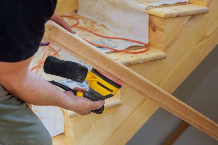 A man is sanding a staircase railing.